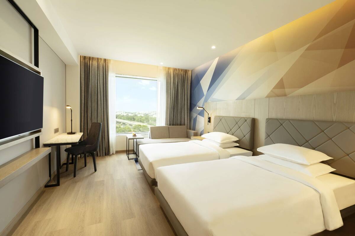 A hotel room with two beds, a desk, a chair, a TV, and a window with curtains.