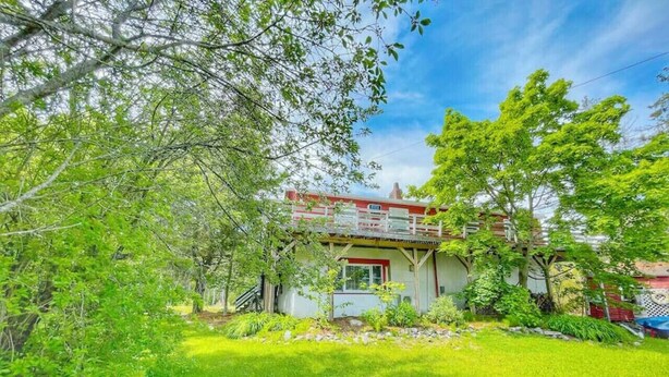 A two-story house with a red roof and white walls, surrounded by lush greenery and trees.