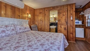 A wooden-paneled room with a bed, a chair, a sink, a mirror, a ceiling fan, and a microwave.