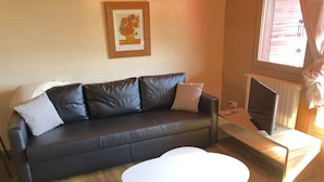Ein Wohnzimmer mit einem dunkelbraunen Ledersofa, weißen Kissen, einem weißen Couchtisch, einem gerahmten Kunstwerk an der Wand und einem Fernseher auf einem Schrank.