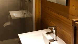Ein modernes Badezimmer mit einer Glaskabine zur Dusche, einer Holzwand und einem weißen Waschbecken mit Spiegel darüber.