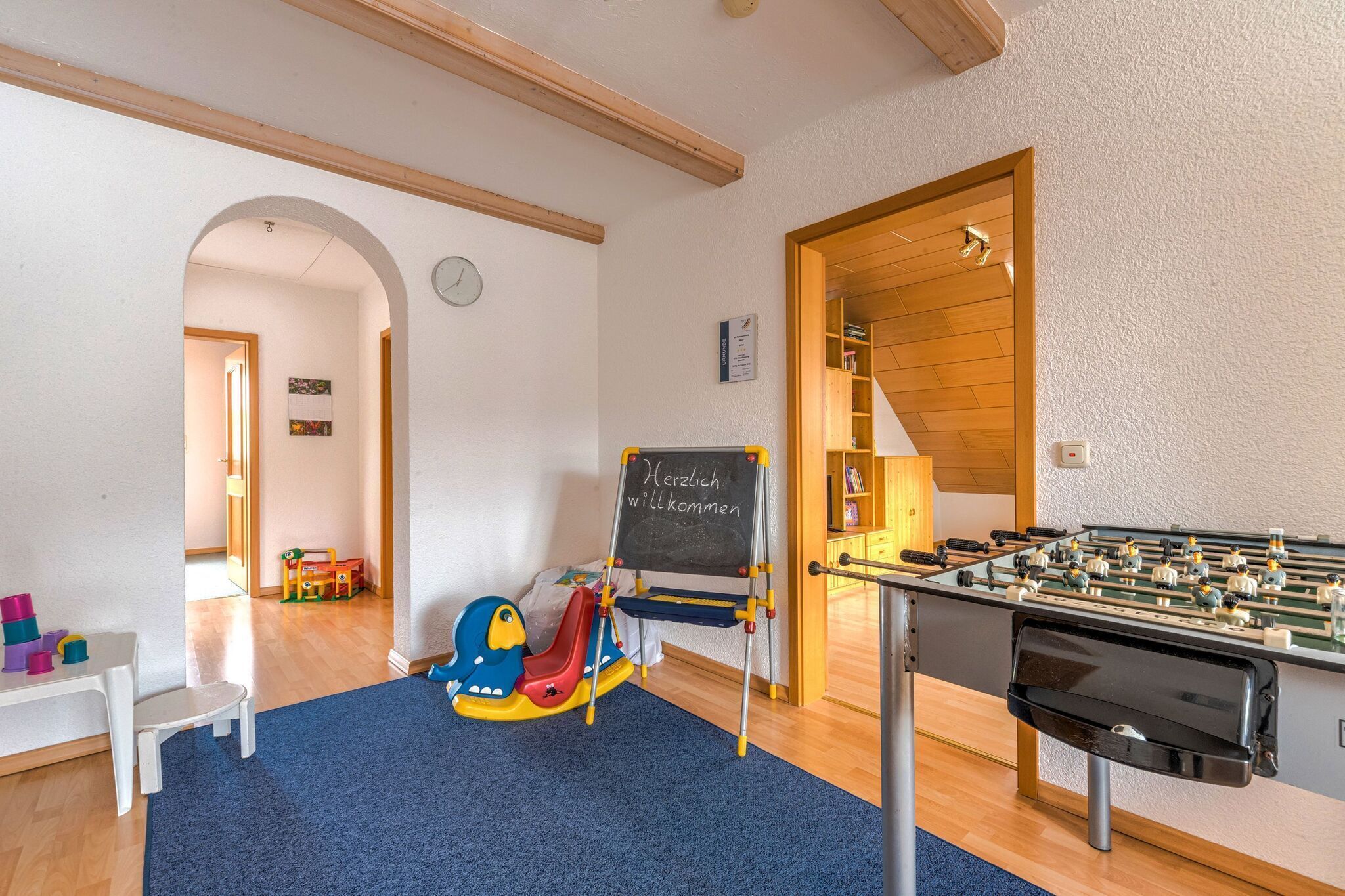 Un espace de jeux pour enfants avec un baby-foot, un toboggan et un tableau noir sur lequel est écrit un message de bienvenue.