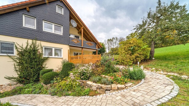 A two-story house with a stone pathway leading to a wooden deck.
