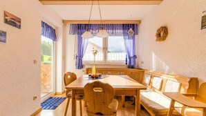 A dining area with a wooden table, chairs, and a bench. There is a window with purple curtains and a view of the outside.