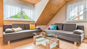 A modern living room with two grey sofas, a glass coffee table, and wooden flooring.