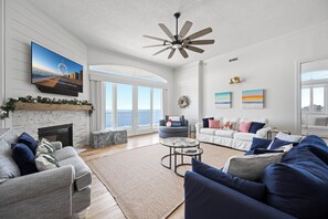A spacious living room with a fireplace, a large TV, and a ceiling fan.