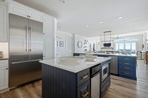 A modern kitchen with stainless steel appliances, a central island, and a view to the living area.