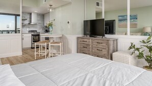 Une chambre moderne avec un grand lit, une télévision et une vue sur la cuisine.