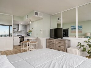 Une chambre moderne avec un grand lit, une télévision et une vue sur la cuisine.
