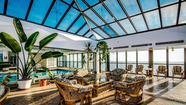 Un vaste espace intérieur doté d’un plafond en verre, de meubles en osier, de plantes en pot et d’une piscine.