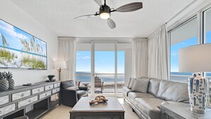 Een ruime woonkamer met een groot raam, een plafondventilator en uitzicht op de oceaan.