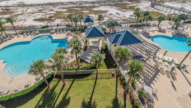Luchtbeeld van een resort met twee grote zwembaden, een strand en een houten looppad.
