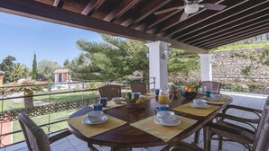 A covered outdoor dining area with a table set for breakfast, overlooking a pool and garden.
