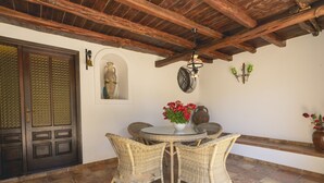 A patio with wicker chairs, a round table, a decorative vase with red flowers, and a wall-mounted light fixture.