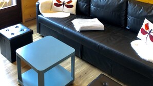 Una habitación acogedora con un sofá de cuero negro, una mesita pequeña y una pared de madera.