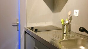 Una cocina compacta con un lavamanos de acero inoxidable, una campana extractora empotrada y una pequeña encimera con utensilios de cocina.