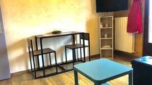 Habitación pequeña con suelo de madera, una mesita, dos sillas, un televisor montado en la pared y un radiador.