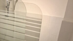 Un baño con ducha envuelta en vidrio, azulejos blancos y un inodoro.