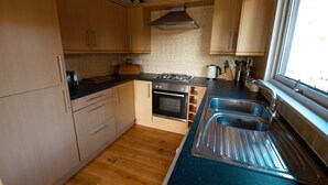 A kitchen with wooden cabinets, a gas stove, an oven, and a sink. - Drummond (Aberfeldy)