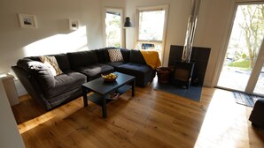 A modern living room with a dark-colored sofa, a small table with a fruit bowl, and a wood-burning stove. - Drummond (Aberfeldy)