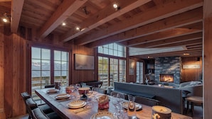 A wooden dining area with a long table set for a meal, a stone fireplace, and a view of the mountains through large windows. - Chalet La Tsoum (Riddes)