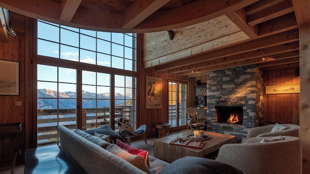 A cozy living room with a stone fireplace, large windows, and a view of mountains. - Chalet La Tsoum (Riddes)