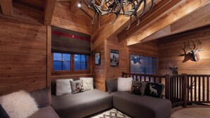 A cozy cabin interior with a sectional sofa, wooden walls, a chandelier, and a mounted deer head. - Chalet La Tsoum (Riddes)