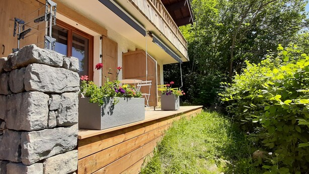 Een houten balkon met stenen muren, buitenmeubels en bloembakken.