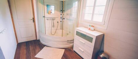 A bathroom with a glass-enclosed shower, a white vanity, and a window.