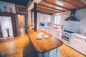 A kitchen with wooden flooring, white cabinets, a central island with pots, a microwave, and a stove.