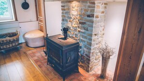 A cozy room with a stone wall, a wooden stove, a wicker basket, and a white toilet. - Fermette Les Ormes - Cottage 8 people in Merlimont village (Merlimont)