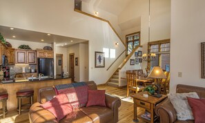 A spacious living area with a leather sofa, wooden dining table, and a staircase leading to an upper level.