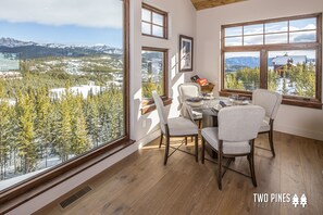 Un coin repas avec une table et des chaises, de grandes fenêtres offrant une vue sur un paysage enneigé et des montagnes.