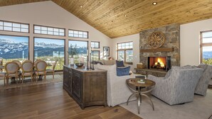 A spacious living room with a fireplace, large windows offering mountain views, and a cozy seating area.