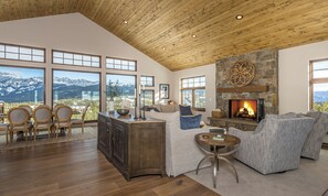 A spacious living room with a fireplace, large windows offering mountain views, and a cozy seating area.