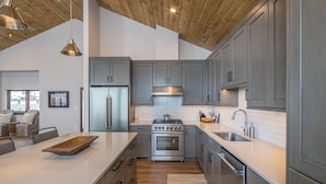 A modern kitchen with grey cabinets, stainless steel appliances, and a wooden ceiling.