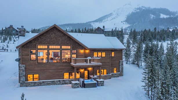 A large wooden cabin with multiple windows, a balcony, and a snow-covered landscape.