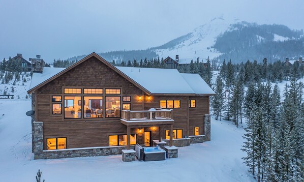 A large wooden cabin with multiple windows, a balcony, and a snow-covered landscape.