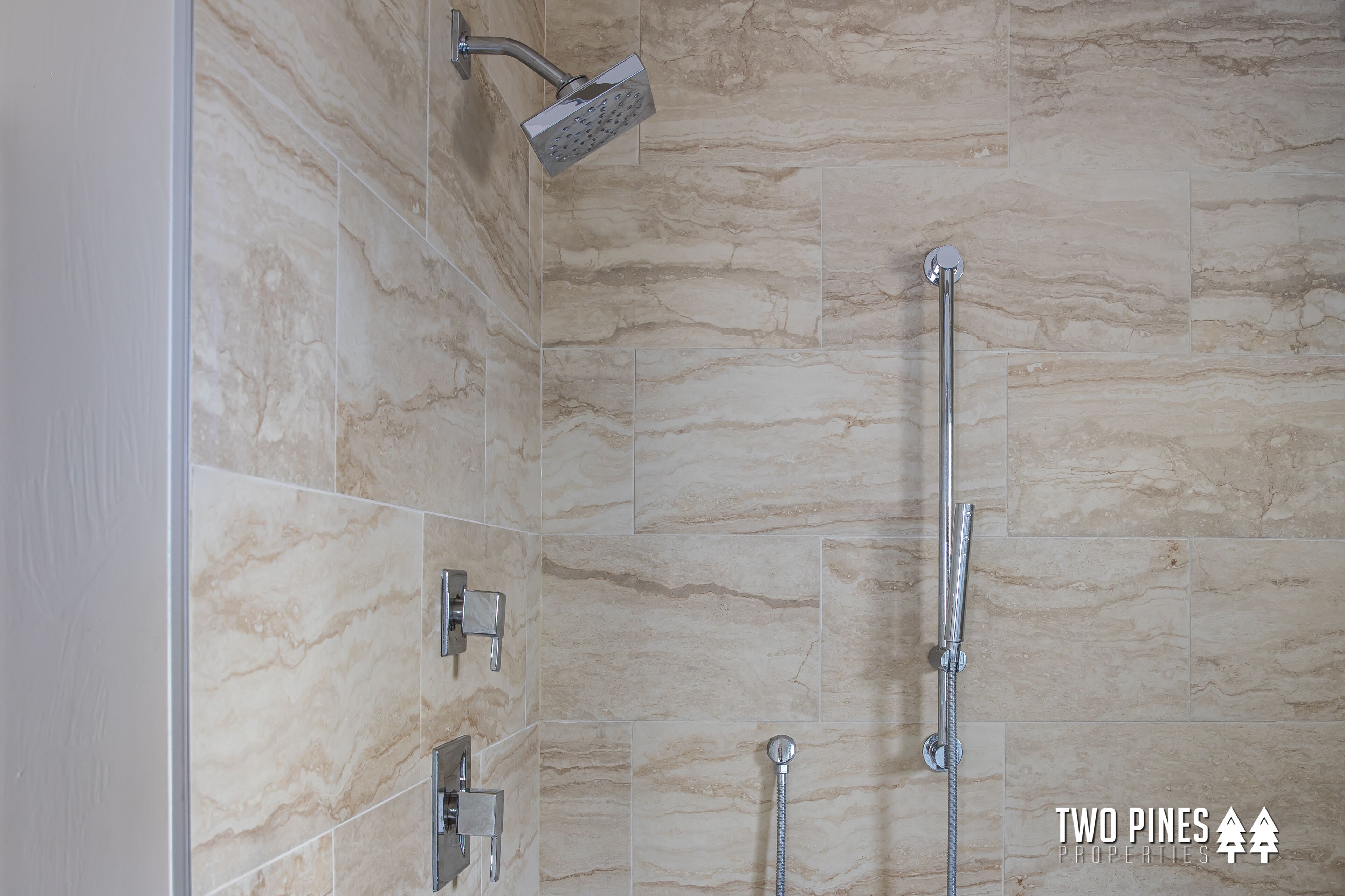A modern bathroom with a shower, a handheld showerhead, and a wall-mounted faucet.