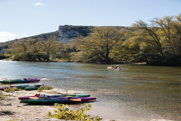 A river with kayaks lined up on the shore and a person kayaking in the distance.