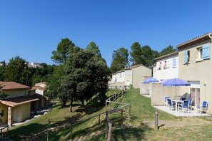 A residential area with houses, a grassy slope, and outdoor seating with umbrellas.