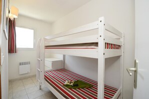 A bunk bed with a striped mattress, a white wall, a window with curtains, and a radiator.