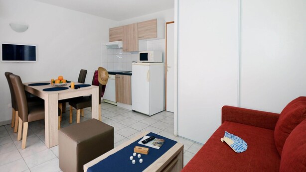 Een kleine woonruimte met een eethoek, kitchenette en een rode bank.