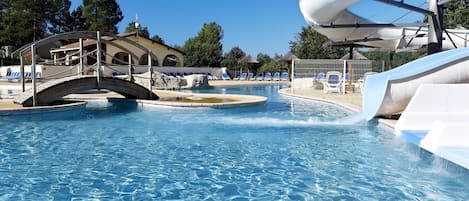 A swimming pool with a water slide, lounge chairs, and a bridge.