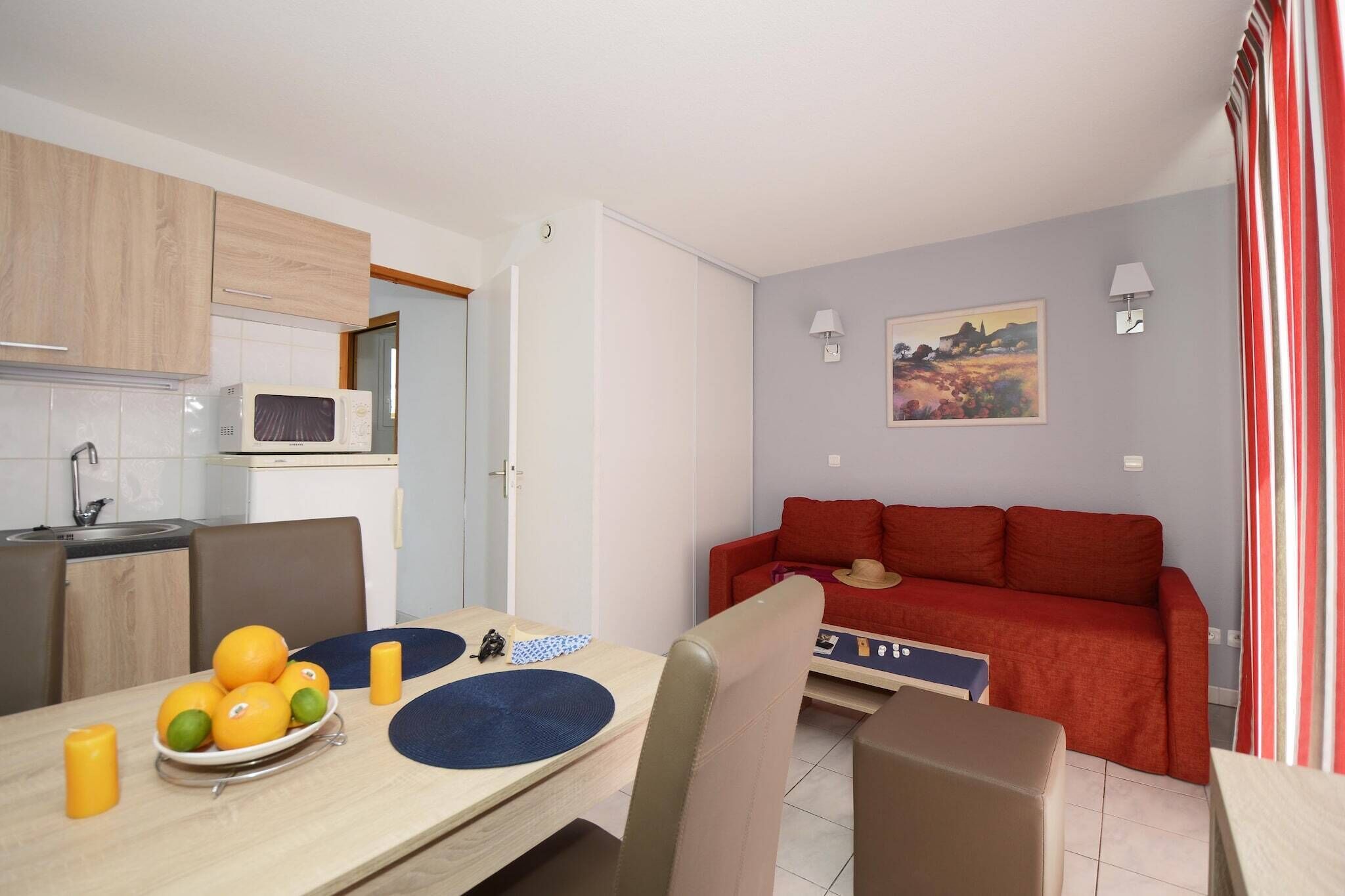 A compact living space with a kitchenette, dining area, and a red sofa.