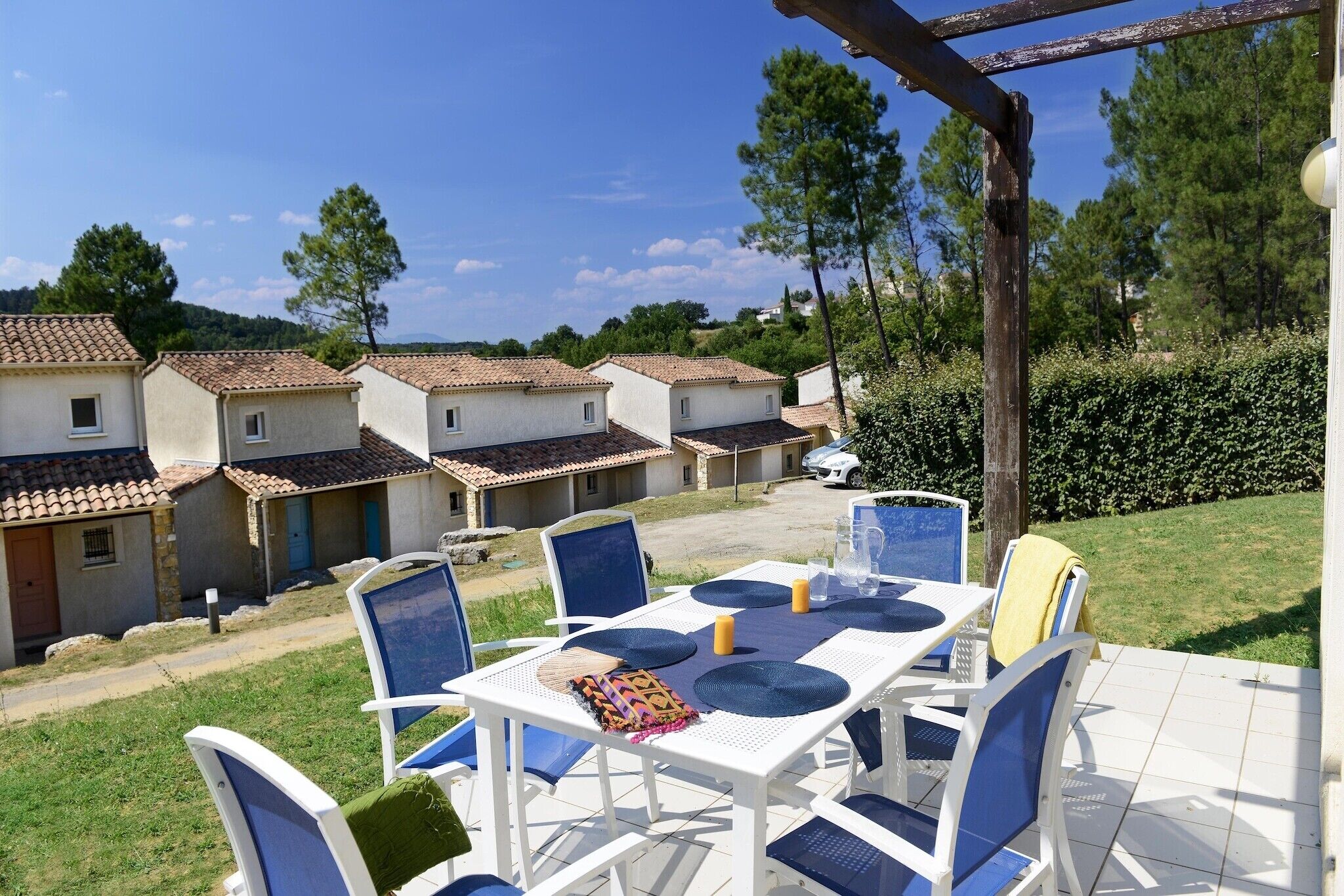 Eine Terrasse mit einem Tisch für zwei Personen, umgeben von Stühlen, in einer Wohngegend mit Häusern im Hintergrund.