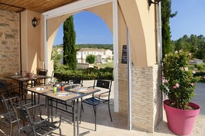 An outdoor dining area with tables and chairs, a chalkboard menu, and a view of the countryside.