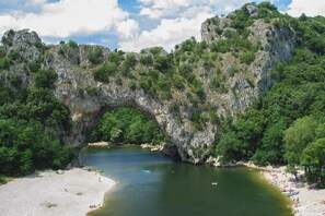 A natural rock arch formation over a body of water with a sandy beach and greenery on the sides. - Cozy Apartment with Terrace (Vallon Pont D Arc)