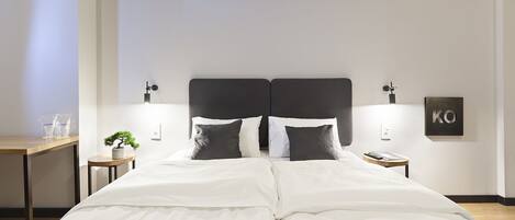 Habitación de hotel con una cama grande, dos mesitas de noche, una planta pequeña y una obra de arte colgada en la pared.