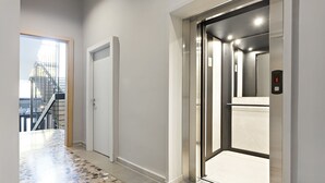 Un pasillo con suelo de baldosas, una puerta cerrada y un ascensor con pantalla digital.